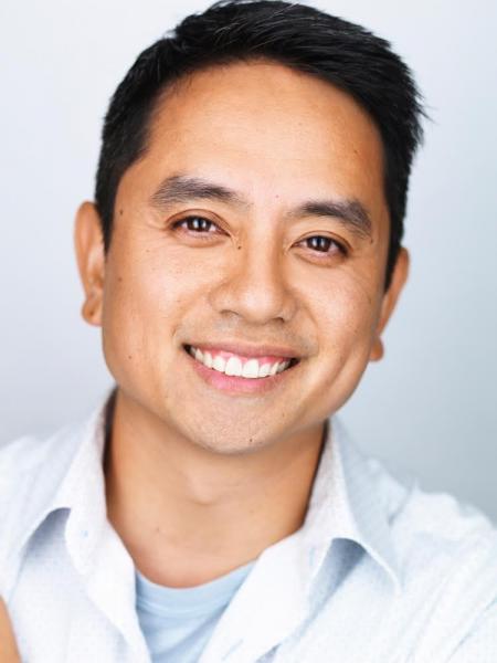 Minh Lê author photo. An Asian man with short black hair wearing a white collared shirt and smiling at the camera. 