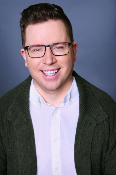 Tom Phillips author photo. A white man with short brown hair wearing glasses a white button up and black jacket.