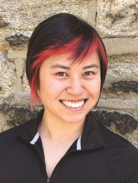 Stephanie Yue photo. An Asian woman with short pixie cut black hair with dyed red bangs wearing a black polo shirt.